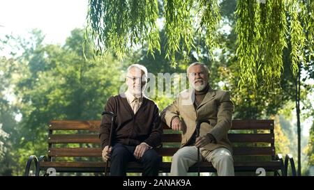 Allegro alti uomini con bastoni da passeggio seduta sul banco, felice della vita nella terza età Foto Stock