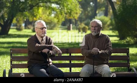 Due uomini anziani con bastoni da passeggio seduto sulla panchina nel parco e pensando a vita Foto Stock
