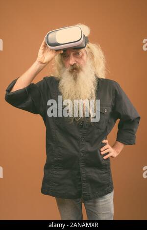 Studio shot di senior uomo barbuto che indossa la maglia nera contro lo sfondo marrone Foto Stock