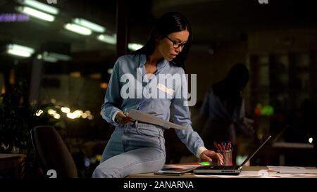 Azienda giovane lavoratore con documenti mano utilizzando portatile per lavorare di notte in ufficio Foto Stock