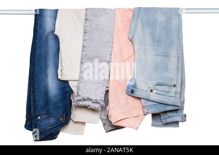 Appendere il jeans isolato. Primo piano della raccolta di cinque femmine vari Pantaloni jeans o pantaloni colorati su un bastone appendiabiti isolato su uno sfondo bianco Foto Stock