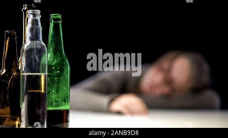 Aprire la bottiglia di alcool sulla tavola con Bevuto donna addormentata sul background e disperazione Foto Stock