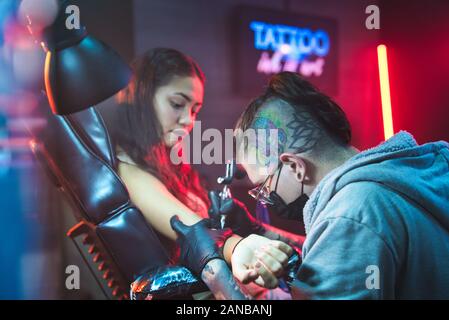 Giovane Donna Ottenere Tatuaggi In Salone Di Bellezza Con Tattoista Di Lavoro Foto Stock