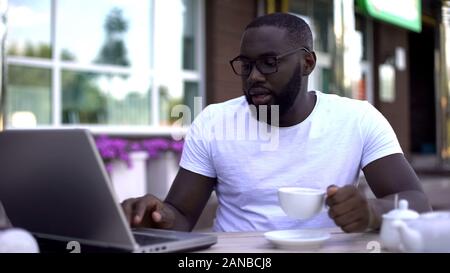 Imprenditore concentrato lavorando su laptop e azienda tazza di caffè nella caffetteria, occupato Foto Stock