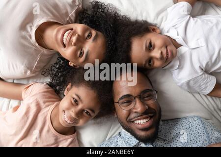 Close up nero felice famiglia di quattro posa sul letto. Foto Stock