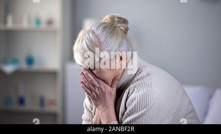 Infelice anziana signora seduta da sola in soggiorno e profondamente il pianto, depressione Foto Stock