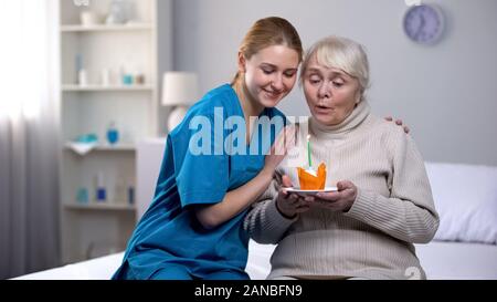 Volunteer abbracciando anziana signora soffiando candela sulla torta di compleanno e servizio ospedaliero Foto Stock