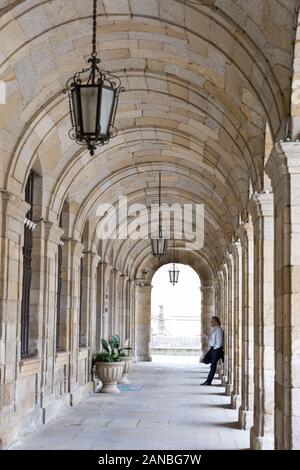 Un uomo fuma una sigaretta nel portico del municipio (Ayuntamiento) a Santiago de Compostela in Spagna. La città si trova il capolinea del Cammino di San Giacomo Foto Stock
