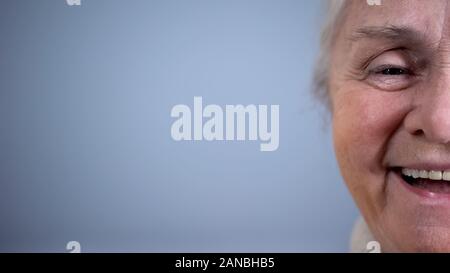 A metà della faccia sorridente vecchia donna sfondo grigio, sicurezza sociale, stato d'animo positivo Foto Stock