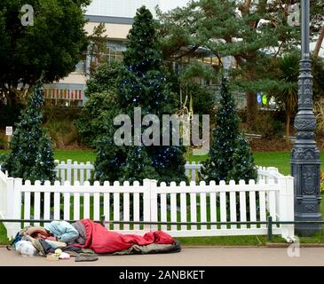 Una persona senza casa dorme accanto ad un albero di Natale nei giardini invernali di Bournemouth Foto Stock