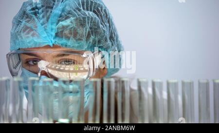 Medical scienziato analizzando reazione biochimica in tubi, esperimento di laboratorio Foto Stock