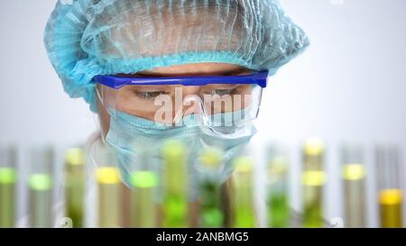 Laboratorio femmina lavoratore nella maschera di protezione e occhiali di sicurezza alla ricerca di campioni Foto Stock