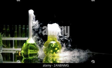 Prodotti chimici liquidi in beute gorgogliamento e emettendo fumo nelle tenebre, reazione Foto Stock