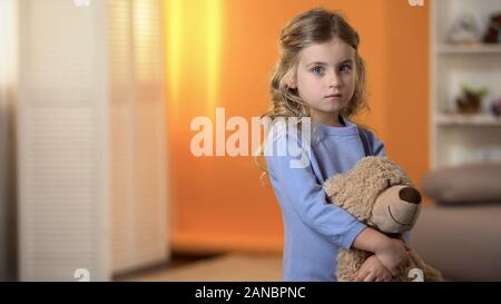 Triste adorabile bambina abbracciando orsetto preferito sentirsi soli in orfanotrofio Foto Stock