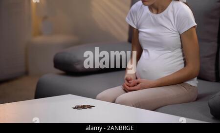 Poveri solitario donna incinta guardando le monete sul tavolo, la mancanza di denaro, depressione Foto Stock