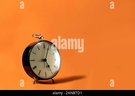 Un wode ritratto di un piccolo vecchio stile antico orologio sveglia con i numeri romani sul quadrante su uno sfondo arancione. Le lancette del cronometro sono pointi Foto Stock