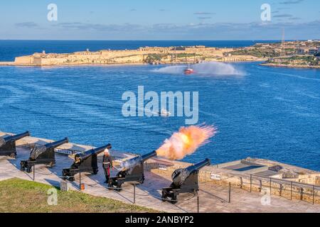 La Valletta, Malta - 9 Gennaio 2020: Colpo di cannone a mezzogiorno in batteria a salve in Upper Barrakka Gardens, con Birgu sullo sfondo, La Valletta, Mal Foto Stock