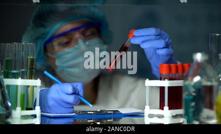 Scienziato tubo di controllo con analisi del sangue e di rendere note, focolaio epidemico Foto Stock