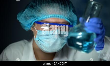 Scienziato analizzando blu trasparente liquido nel pallone, acqua metalli pesanti checkup Foto Stock