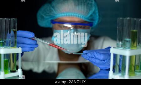 Ricercatore di gocciolamento sostanza arancione sul test di vetro, studiando le proprietà del liquido Foto Stock