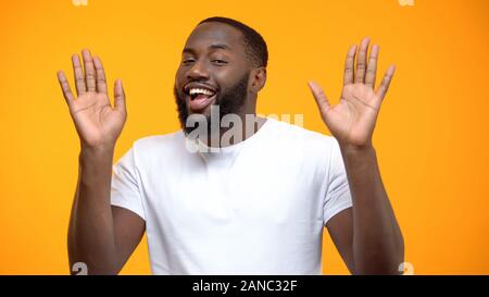 Sorridente uomo afro-americano che mostra le palme aperte, dando il massimo, sfondo giallo Foto Stock