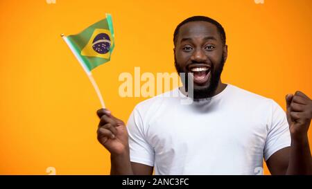 Felice l'uomo nero azienda bandiera brasiliana, tifoso di supporto squadra nazionale Foto Stock