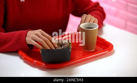 Giovane donna prendendo vetrato ciambella di cioccolato da box, caffè sul tavolo, dessert Foto Stock