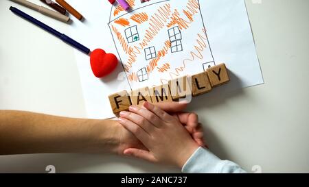 Bambino tenendo la mano della persona adulta, famiglia parola fatta dai cubi sulla foto della casa Foto Stock