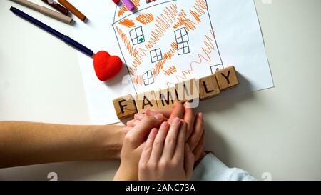 Kid tenendo la mano della persona adulta, famiglia parola fatta dai cubi sulla foto della casa Foto Stock