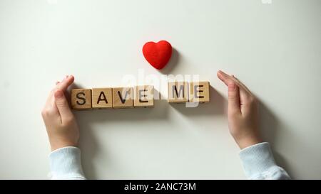 Childs mettendo mano cuore segno e salvare me frase composta di cubi di legno, carità Foto Stock