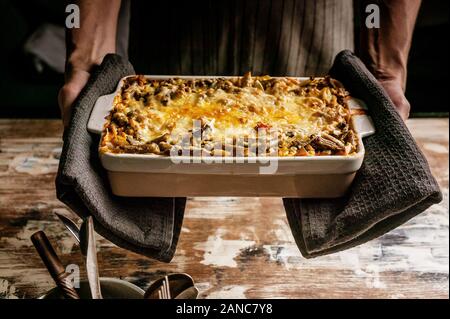 Mani femminili in attesa di piatti in ceramica con lasagne alle verdure con fagiolini e formaggio. Una sana alimentazione vegetariana. Foto Stock