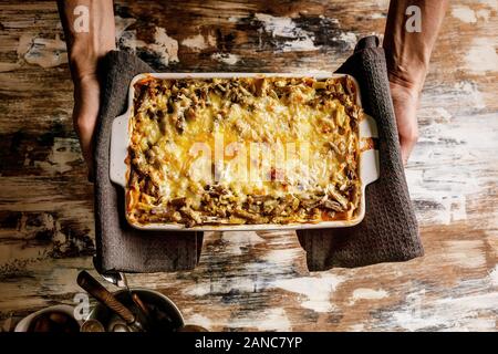 Mani femminili in attesa di piatti in ceramica con lasagne alle verdure con fagiolini e formaggio. Una sana alimentazione vegetariana. Foto Stock