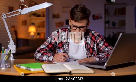 Studente concentrato in bicchieri facendo il suo hometask, lavorando sul progetto scuola Foto Stock