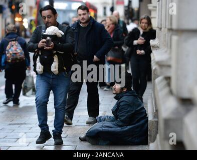 Un uomo che porta un bambino e utilizzando il suo telefono mobile passa da un senzatetto in Victoria, Londra. Foto di PA. Picture Data: giovedì 16 gennaio, 2020. Foto di credito dovrebbe leggere: Nick Ansell/PA FILO Foto Stock