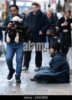 Un uomo che porta un bambino e utilizzando il suo telefono mobile passa da un senzatetto in Victoria, Londra. Foto di PA. Picture Data: giovedì 16 gennaio, 2020. Foto di credito dovrebbe leggere: Nick Ansell/PA FILO Foto Stock