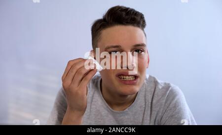 Adolescente turbato il trattamento di ferita con liquido antisettico guardando la telecamera, accigliata Foto Stock