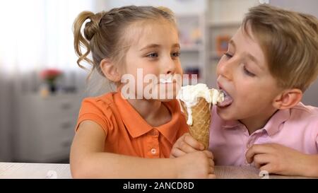 Adorabili e un ragazzo e una ragazza di mangiare il gelato insieme, seduti al tavolo di casa, cibo Foto Stock