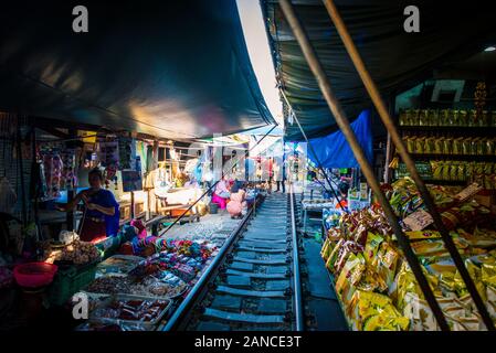 Mae Klong/Thailand-08December2019: Stazione ferroviaria Mae Klong con piste e treno che passa attraverso il mercato giornaliero con venditori di tutto. Foto Stock