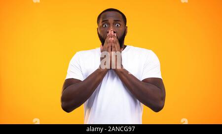 Giovani sorpresi uomo nero chiudendo la bocca con le mani su sfondo giallo Foto Stock