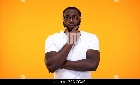 Smart giovane studente nero in bicchieri pensando di rispondere, sfondo giallo Foto Stock