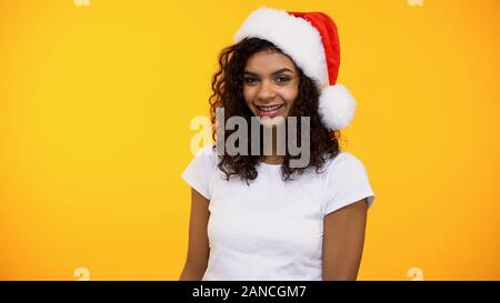 Piuttosto giovane femmina in santa hat sorridente sulla fotocamera su sfondo luminoso, party Foto Stock