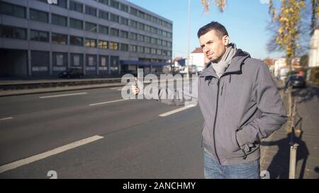 Giovane uomo la cattura di automobile in città sconosciuta e a buon mercato viaggiare, autostop Foto Stock