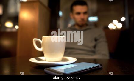 Maschio solitario in seduta cafe, telefono giacente sul tavolo, in attesa che la moglie in data Foto Stock