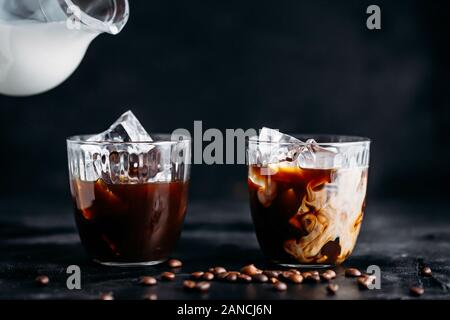 Versare il latte in un bicchiere di caffè espresso con ghiaccio Foto Stock