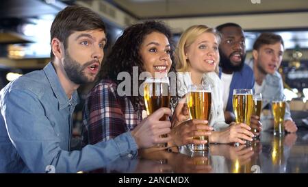 I ventilatori di sport di holding bicchieri da birra attentamente guardare la competizione sportiva in pub Foto Stock