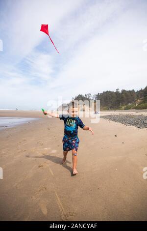 Giovane ragazzo che corre con aquilone sulla spiaggia della costa dell'Oregon. Foto Stock