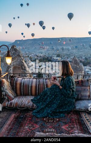 Donna che beve il tè del mattino presto con palloncini ad aria calda in Cappadocia Foto Stock