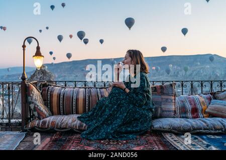 Donna che beve il tè del mattino presto con palloncini ad aria calda in Cappadocia Foto Stock