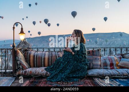 Donna che beve il tè del mattino presto con palloncini ad aria calda in Cappadocia Foto Stock