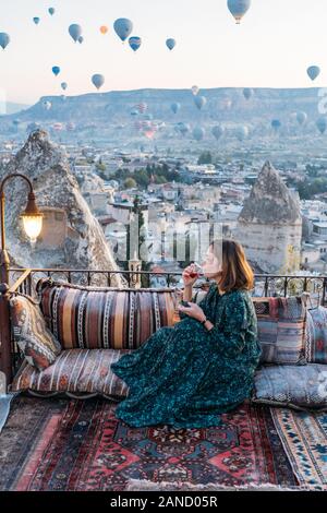 Donna che beve il tè del mattino presto con palloncini ad aria calda in Cappadocia Foto Stock